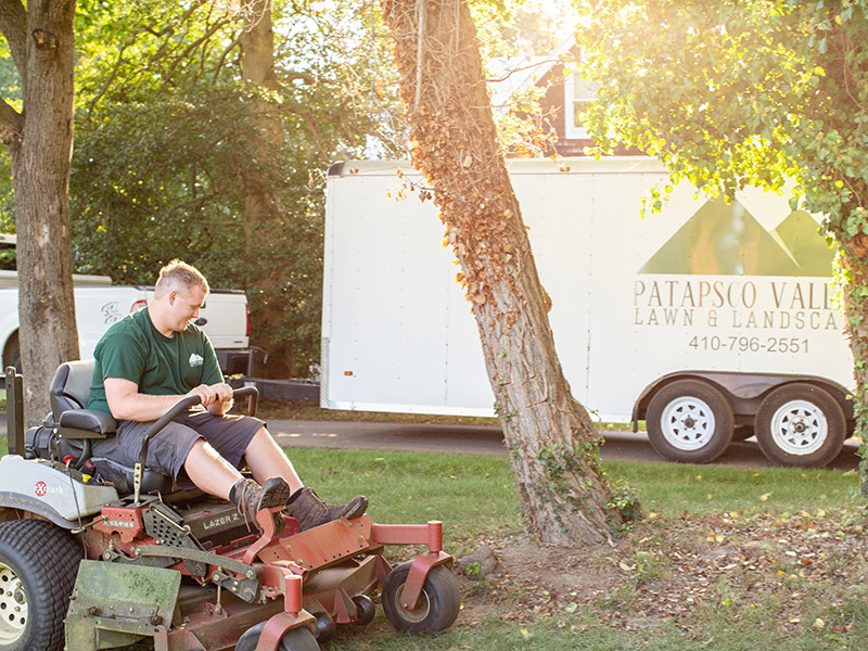 Ronnie on a mower with a Patapsco Valley Lawn & Landscape trailer in the background